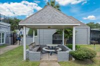 Charming outdoor gazebo with cozy seating and picnic table, surrounded by lush greenery and a bright blue sky.