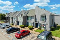 Charming townhouse complex with modern brick facade, lush greenery, and ample parking under a vibrant blue sky.