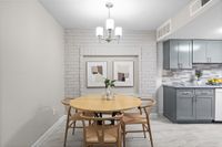 Charming dining area with round wooden table, modern grey kitchen cabinets, and stylish art on a white brick wall.