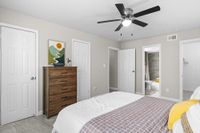 Inviting bedroom with modern ceiling fan, wooden dresser, and tasteful wall art, featuring an ensuite bathroom and ample closet space.