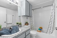 Modern bathroom showcasing elegant granite countertop, sleek fixtures, and minimalist decor. Features a stylish shower with patterned curtain, accentuated by charming plants and neatly arranged essentials. Ideal for relaxation and convenience.