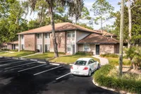 Apartment building brick exterior and parking spaces. Trees and shrubbery surround exterior