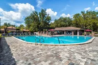 Blue curved pool with brick walkway surrounding. Lounge chairs and umbrellas in the background