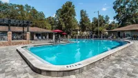 Blue curved pool with brick walkway surrounding. Lounge chairs and umbrellas in the background