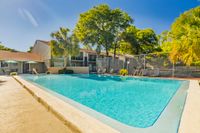 Community pool with apartment building, tennis court, and trees in the background.
