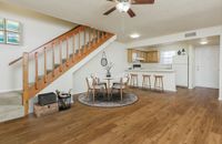 Living room with hardwood floors, carpeted stairs, white walls, and passthrough to the kitchen.
