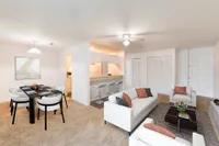 Carpeted living and dining area with white and black furniture, grey area rug, and a passthrough to the kitchen.