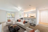 Carpeted living and dining area with white and black furniture, grey area rug, and a passthrough to the kitchen.