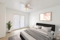 Carpeted bedroom with modern furniture including two end tables, two lamps, bed, potted plant, and two doors leading to an outdoor balcony.
