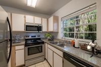 Tiled floor kitchen with white and exposed cabinets, stainless steel appliances and granite like countertops.