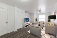 Living area with hardwood floors, white walls, modern furniture, and a staircase. There are two chairs, 1 couch, coffee table and a white media center.