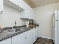Galley kitched with white cabinets, double sink, and white refrigerator.