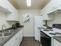 Galley kitchen with white cabinets, double sink, and white refrigerator and stove..