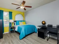 Bedroom with ceiling fan and furniture with yellow accent wall.