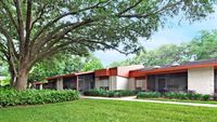 Single level buildings with large tree, lush landscaping in foreground.