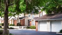 Front of apartment buildings including two garage doors and a large tree on the right.