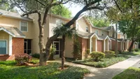 Front of townhomes with lush landscape and trees.