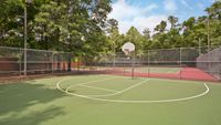 Half basketball court with tennis court and trees in background.
