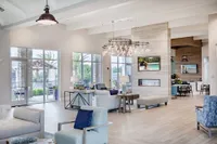 Resident lounge with large windows, chairs and couches, and a wall mounted television and fireplace.