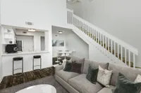 Living area looking into kitchen, breakfast bar with two stools, and a stairway on the right.