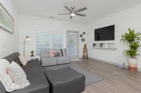 Living room with wall mounted television, hardwood floors, area rug, grey couch, window, and access to balcony.