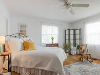 Bedroom with ceiling fan, two windows, hardwood floors, bed, end table with lamp, and area rug.