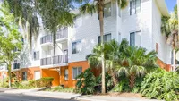 Exterior of three floor building with tall palm and lush landscaping.