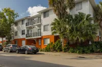 Exterior view of The Avenues building. There are cars parked in front and the building is painted orange and has white siding.