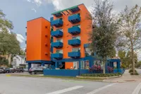 Exterior of the Orange and Blue building. There is a road in front that leads to covered parking and a sidewalk that wraps around the building.