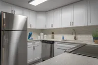 Kitchen with wood style floor, white cabinets, stainless steel appliances, white subway tile, white quartz countertops, a coffee machine and other items.