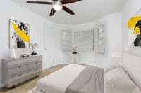 Bedroom with bay window, bed, ceiling fan, night stand.