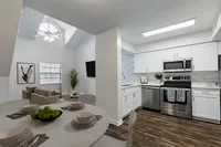 Kitchen with wood floors, premium appliances, dining table in foreground. Background is living room with vaulted ceiling, couch and TV