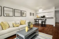 Living room with cream couch and coffee table. Dining set and breakfast bar visible in background.