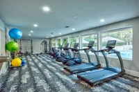 Fitness center with various cardio equipment and wall mounted television.  Mirrored wall in the background.