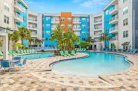Community pool area with hammock in foreground, green lounge chairs and residential buildings in the background.