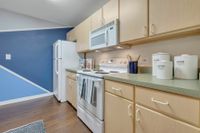 Kitchen with wood cabinets, green countertops, and white appliances. There is a laundry room in the background with a blue accent wall.