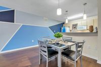 Wide shot of the dining area with a square table and chairs, and living area in the background with a couch. There are hardwood floors and white and blue walls.