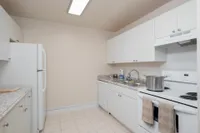 Galley kitchen with white cabinets, double sink, and white refrigerator and stove..