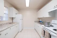 Galley kitchen with white cabinets, double sink, and white refrigerator and stove..