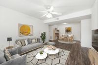 Living room with hardwood style floors, large area rugs, white couch, light wood table with yellow chairs, and the entry to the kitchen in the background.