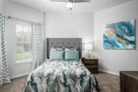 Carpeted bedroom with fluffy comforter and pillows on bed. Bay window on far side with wall painted green.
