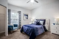 Carpeted bedroom with fluffy comforter and pillows on bed. Bay window on far side with wall painted green.