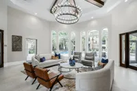 Large foyer with loveseats and lounge chairs underneath a chandelier. Also present is a large wall mounted tv above a fireplace and a small kitchen with a coffee station.