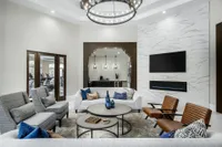 Large foyer with loveseats and lounge chairs underneath a chandelier. Also present is a large wall mounted tv above a fireplace and a small kitchen with a coffee station.