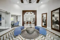 Large foyer with loveseats and lounge chairs underneath a chandelier. Also present is a large wall mounted tv above a fireplace and a small kitchen with a coffee station.