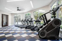 Carpeted fitness center with cardio equipment including treadmills and stationary bicycles overlooking community pool.