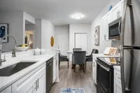 Galley style kitchen with white cabinets, black appliances, under-mount sink, and dining table in the background.