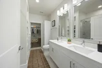 Modern bathroom with dual sinks, large mirror, and a walk-in closet featuring organized storage.