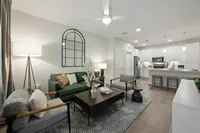Modern open-plan living room with a green sofa, stylish armchairs, and a spacious kitchen in view.