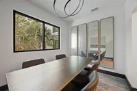 Chic dining room with large table, stylish chairs, and a modern circular light fixture, featuring a scenic view of lush greenery through the window.